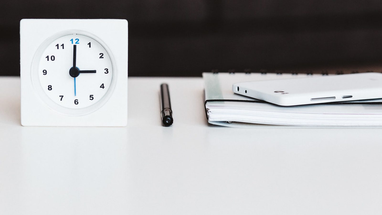 A clock and notebook on a clear desk